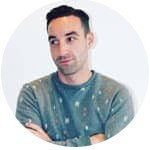 DCP klant portretfoto Portretfoto van een man met korte donkere haren en grijze trui, met armen over elkaar, kijkt opzij voor een witte achtergrond – voorbeeld van een DCP klant.