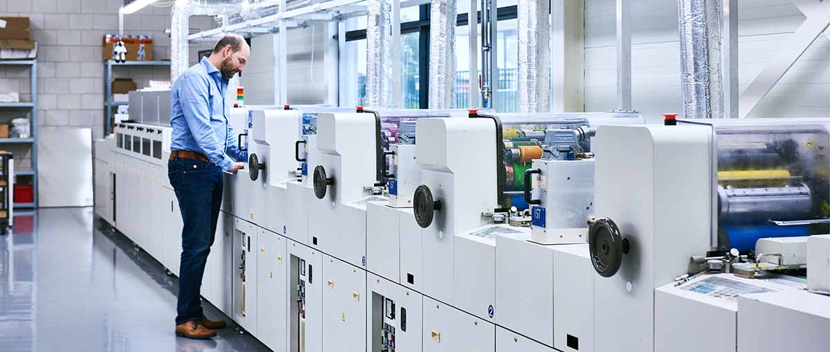 DCP drukkerij en productiefaciliteit Productieruimte van DCP met medewerkers en geavanceerde druk- en verwerkingsmachines voor plastic passen en labels.