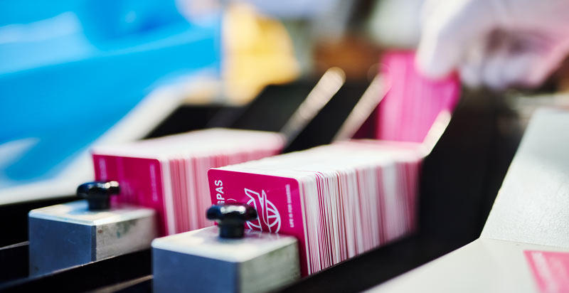 Productieproces van plastic klantenpassen in een gespecialiseerde print- en verwerkingsmachine. Close-up van een hand met handschoen die roze klantenpassen verwerkt in een machine voor het bedrukken of sorteren van plastic kaarten.