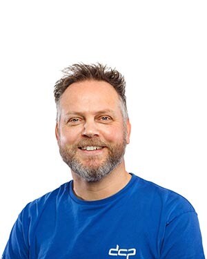 Portret van DCP medewerker Tonny Draijer in donkerblauwe bedrijfskleding met DCP-logo, lachend met armen over elkaar. DCP medewerker Tonny Draijer