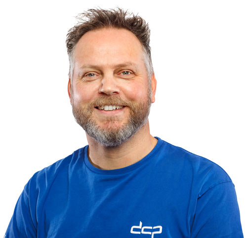 Portret van een DCP medewerker in donkerblauwe bedrijfskleding met het DCP-logo, lachend met armen over elkaar. DCP medewerker in bedrijfskleding